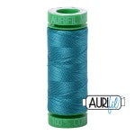 Spool of teal thread with green cap on a white background