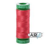 Red spool of thread with a green cap on a white background