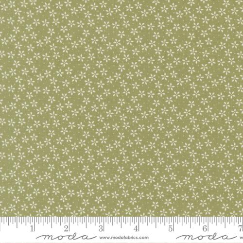 Fabric pattern with small white flowers on a green background, featuring a ruler for scale.