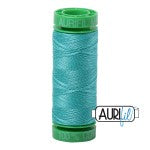 Turquoise spool of thread with a green cap on a white background