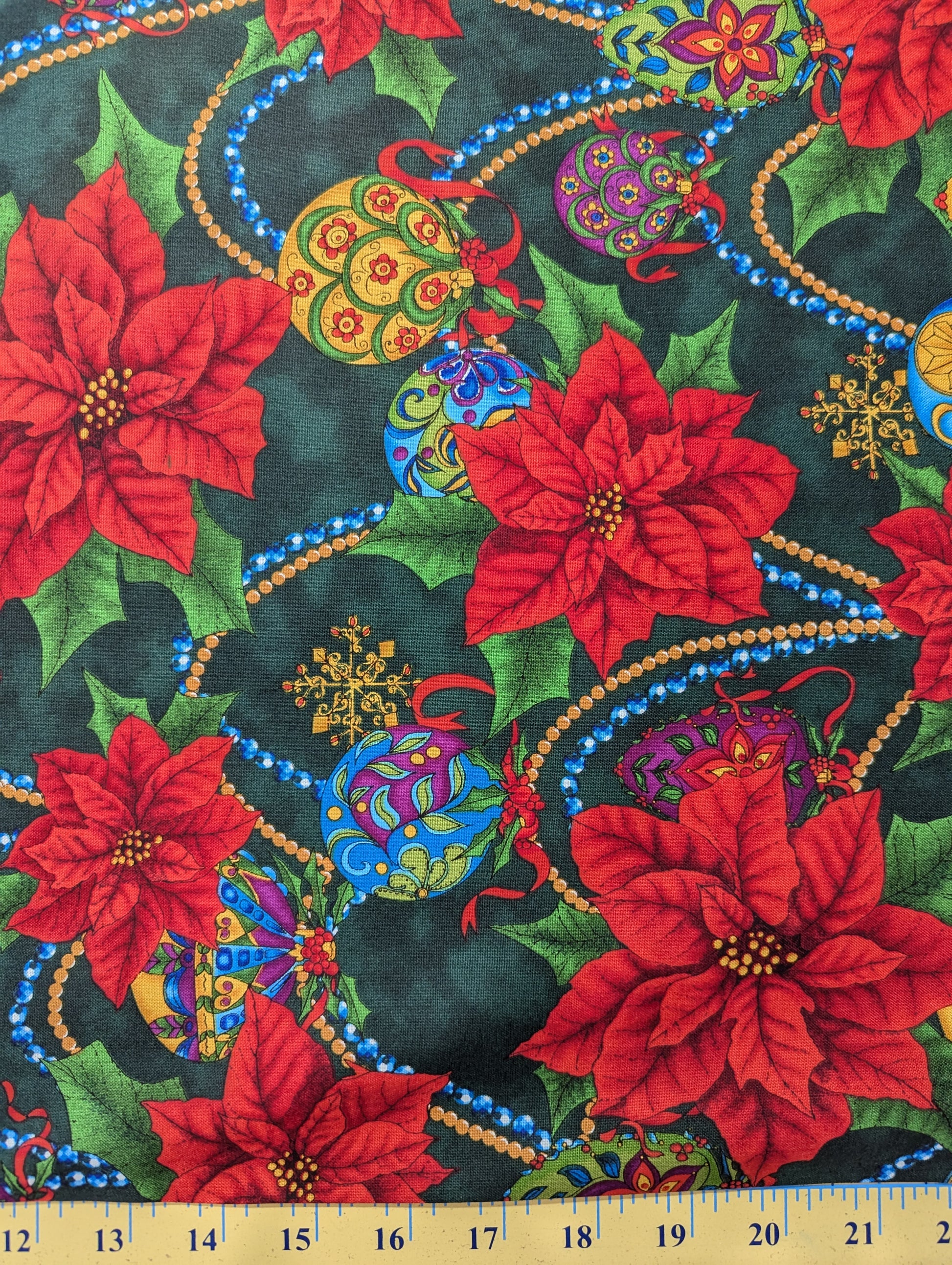 Colorful fabric with red poinsettias, Christmas balls, and decorative elements on a dark background.