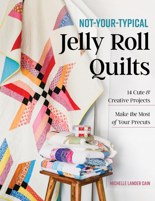 Colorful jelly roll quilt on a wooden stool with book cover text 'Not-Your-Typical Jelly Roll Quilts' by Michelle Lander Cain.